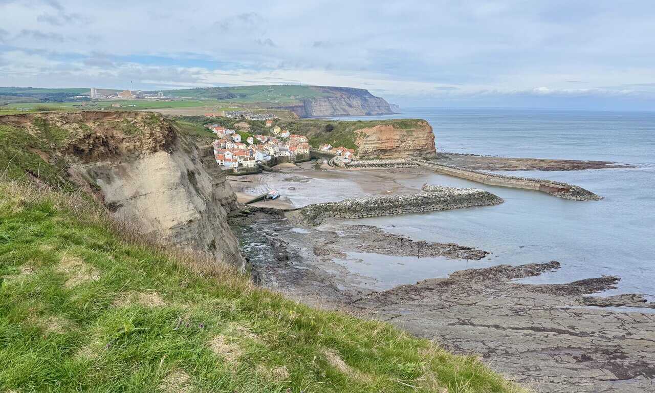 Staithes Harbour comes into view on the Runswick Bay circular walk with cottages, boats and breakwaters below.