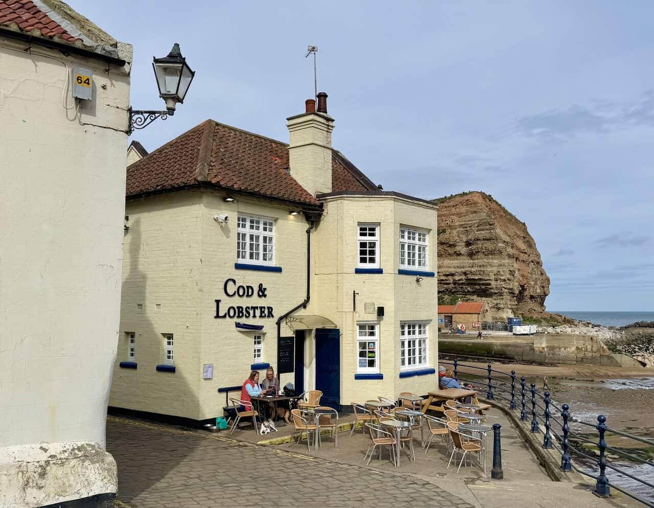 The Cod and Lobster stands at the water’s edge in Staithes with cottages and cliffs nearby.
