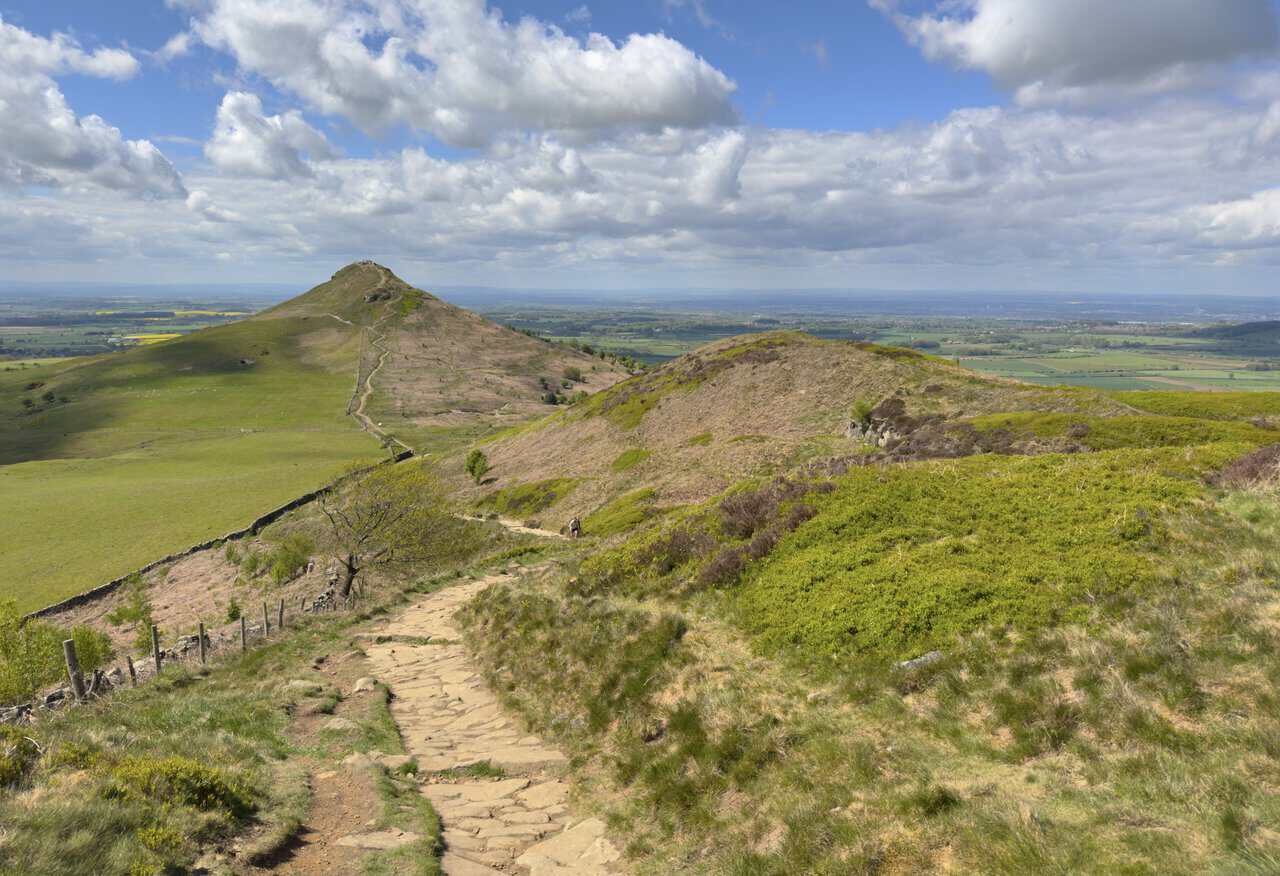 A stone conservation path follows the Cleveland Way past Little Roseberry, with Roseberry Topping rising ahead and walkers on the summit.
