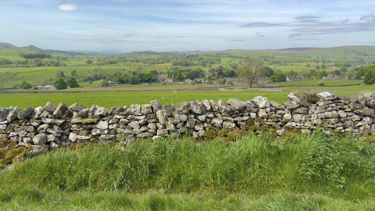 View from High Lane on the Hebden circular walk, looking across dry stone walls towards the rooftops of Grassington with Pendle Hill faintly visible on the horizon.
