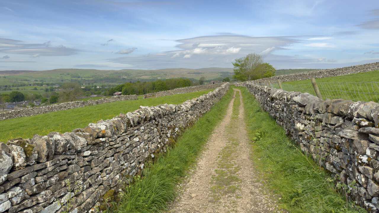 The broad stone track of High Lane between dry stone walls, leading north-west towards Grassington on this Hebden walk.