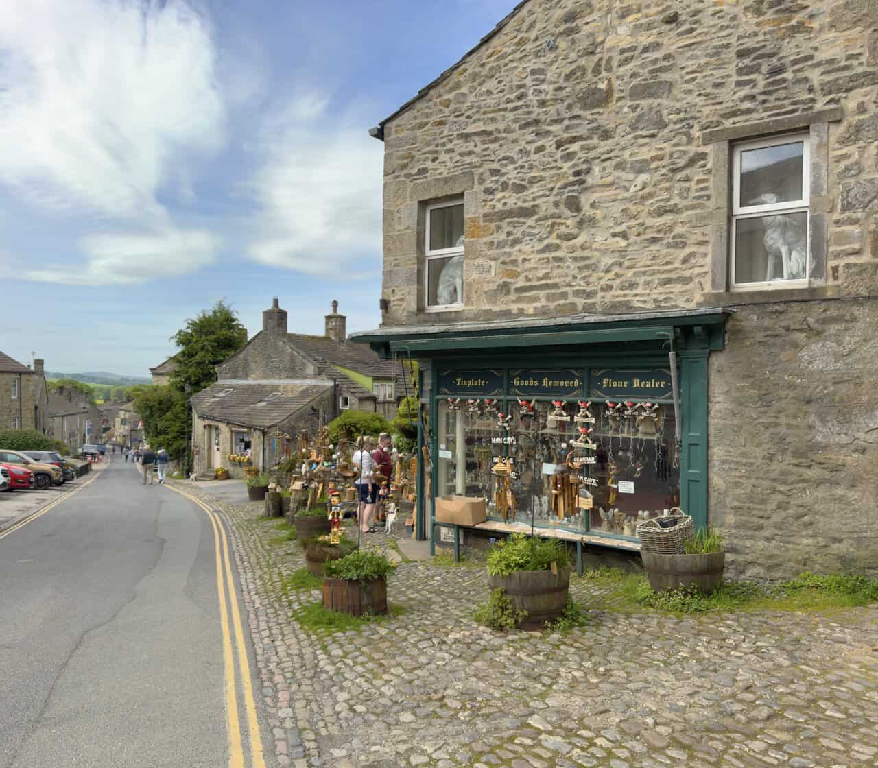 Cobbled Main Street in Grassington with traditional shopfronts, including a craft shop in a former tinplate and flour dealer's premises.