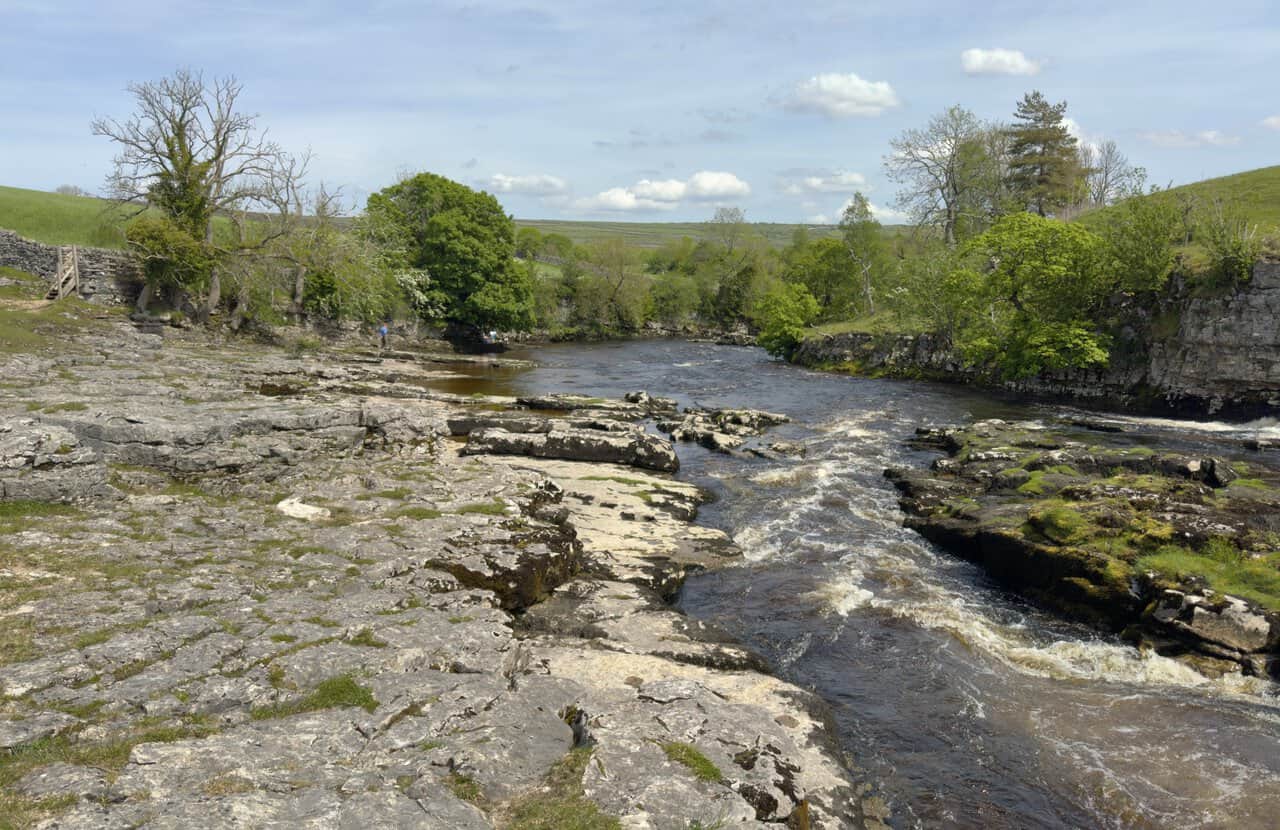 The full sweep of Ghaistrill's Strid on the River Wharfe, with the river curving past pale limestone slabs and small rapids.