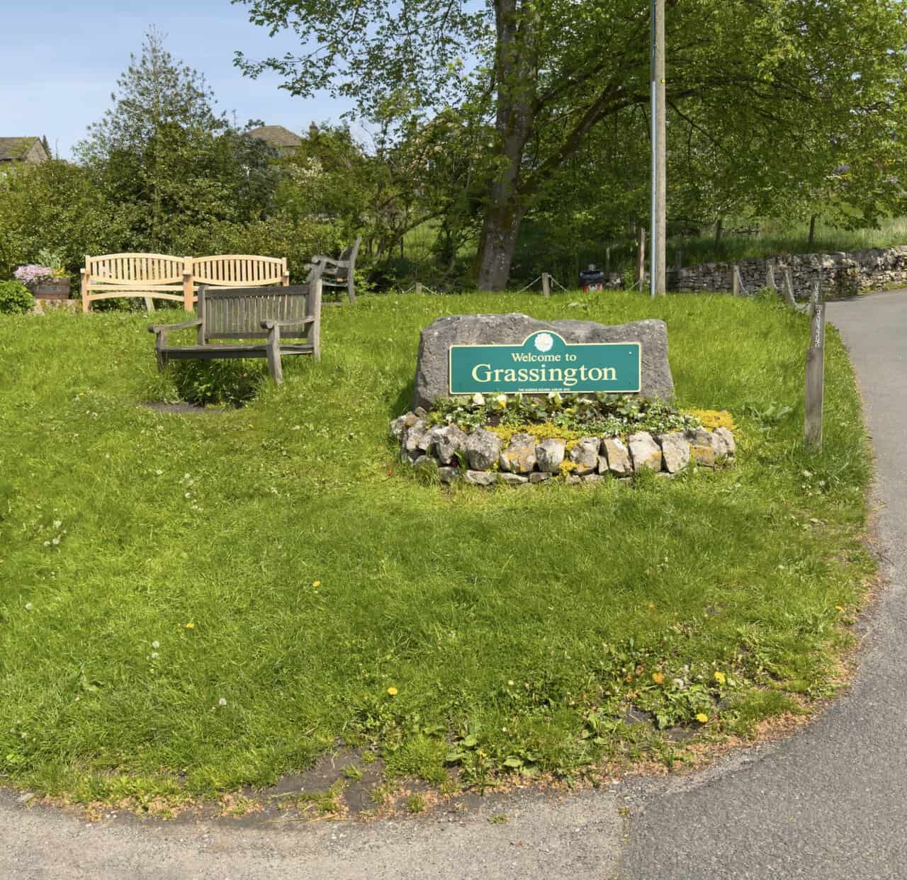 The 'Welcome to Grassington' stone and wooden benches set on a grassy area at the western entrance to the village.