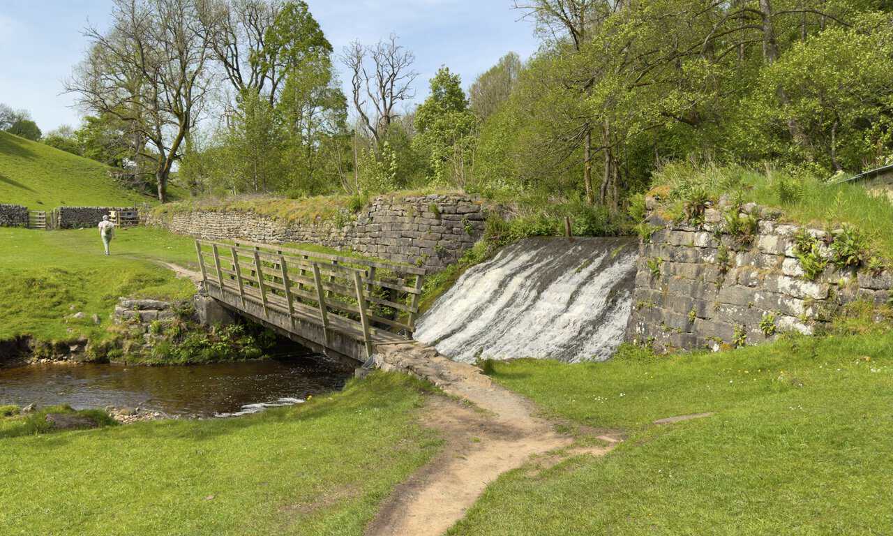 Wooden footbridge across Hebden Beck beside a small weir, on the path back to Hebden village on this Hebden walk.