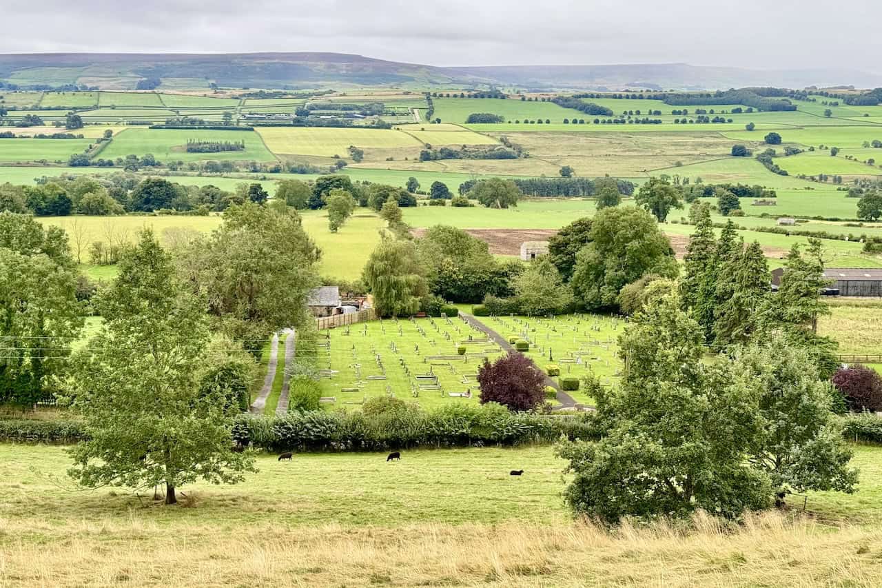 A patchwork of green fields stretches across the floor of Wensleydale, as seen from the limestone terrace of the Leyburn Shawl.