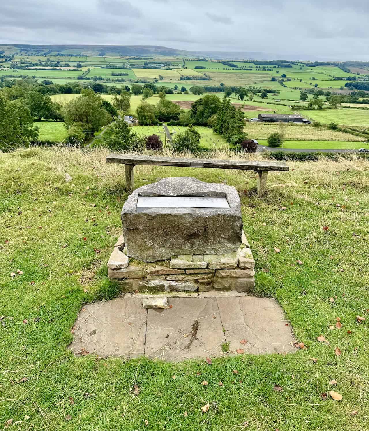 A stone topographical map sits beside a bench on the Leyburn Shawl, highlighting visible landmarks including the River Ure, Little Whernside, Penhill, and Addlebrough.