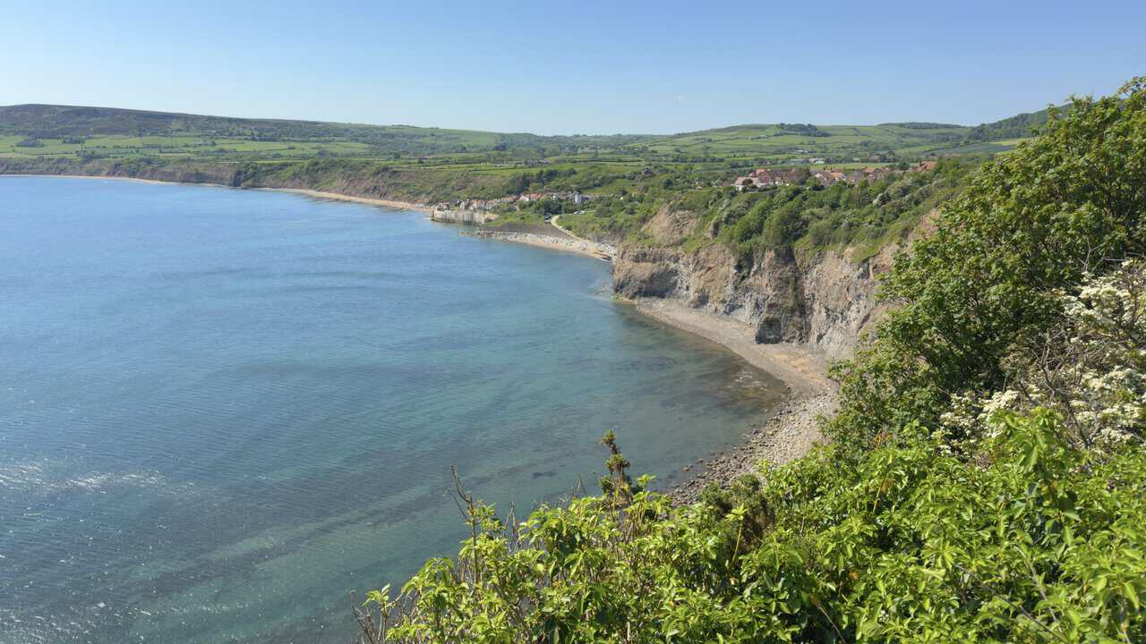 A wide coastal view across Robin Hood's Bay from the Cleveland Way, with the village on the far headland and blue sea below.