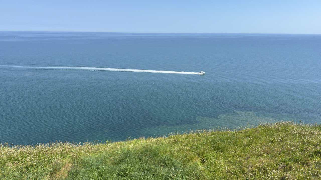 A small boat crosses the calm sea below the clifftop path near the Cow & Calf on the Whitby walk.
