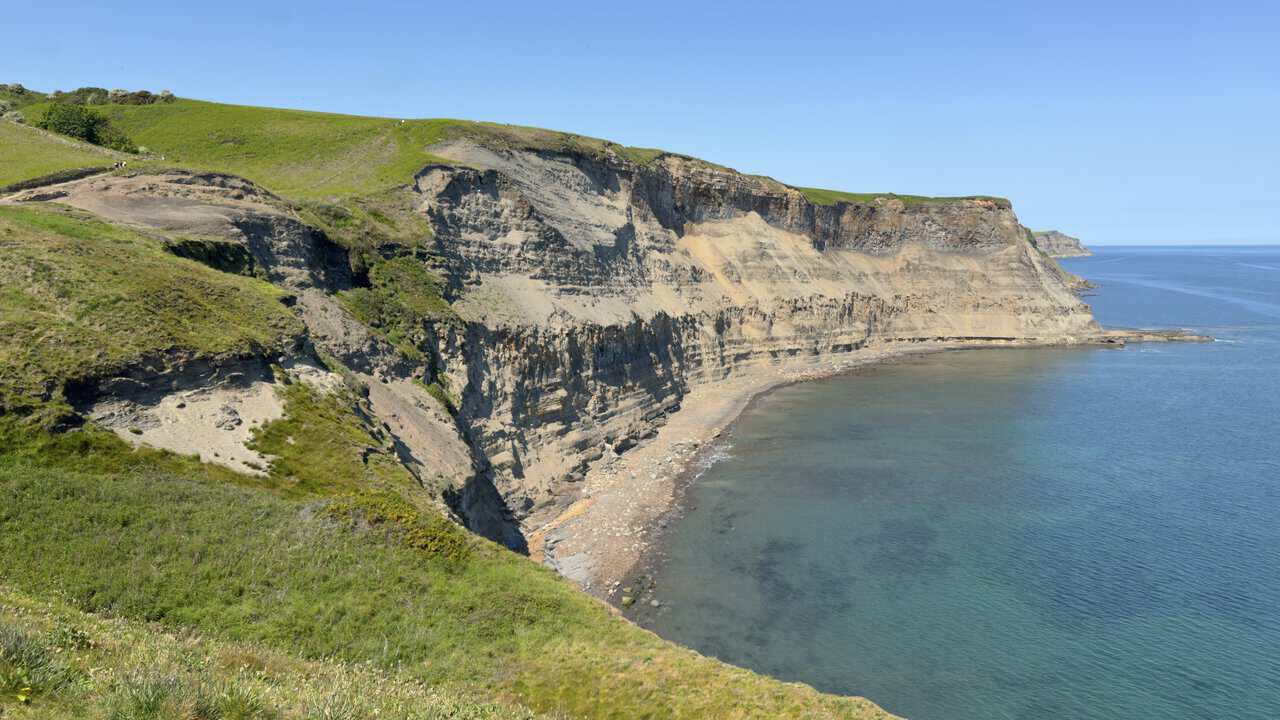 Dark layered cliffs drop to the beach at Far Jetticks on the Whitby walk, where shale seams linked with Whitby jet can still be seen.