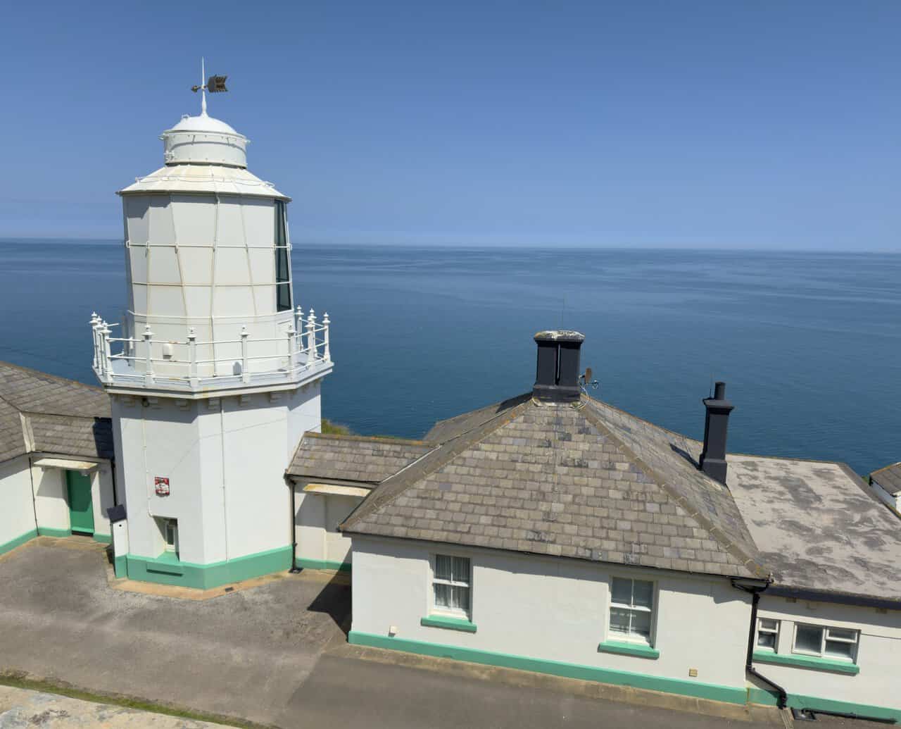 A close view of Whitby Lighthouse shows the lantern, white balcony railings and weathervane above the tower.