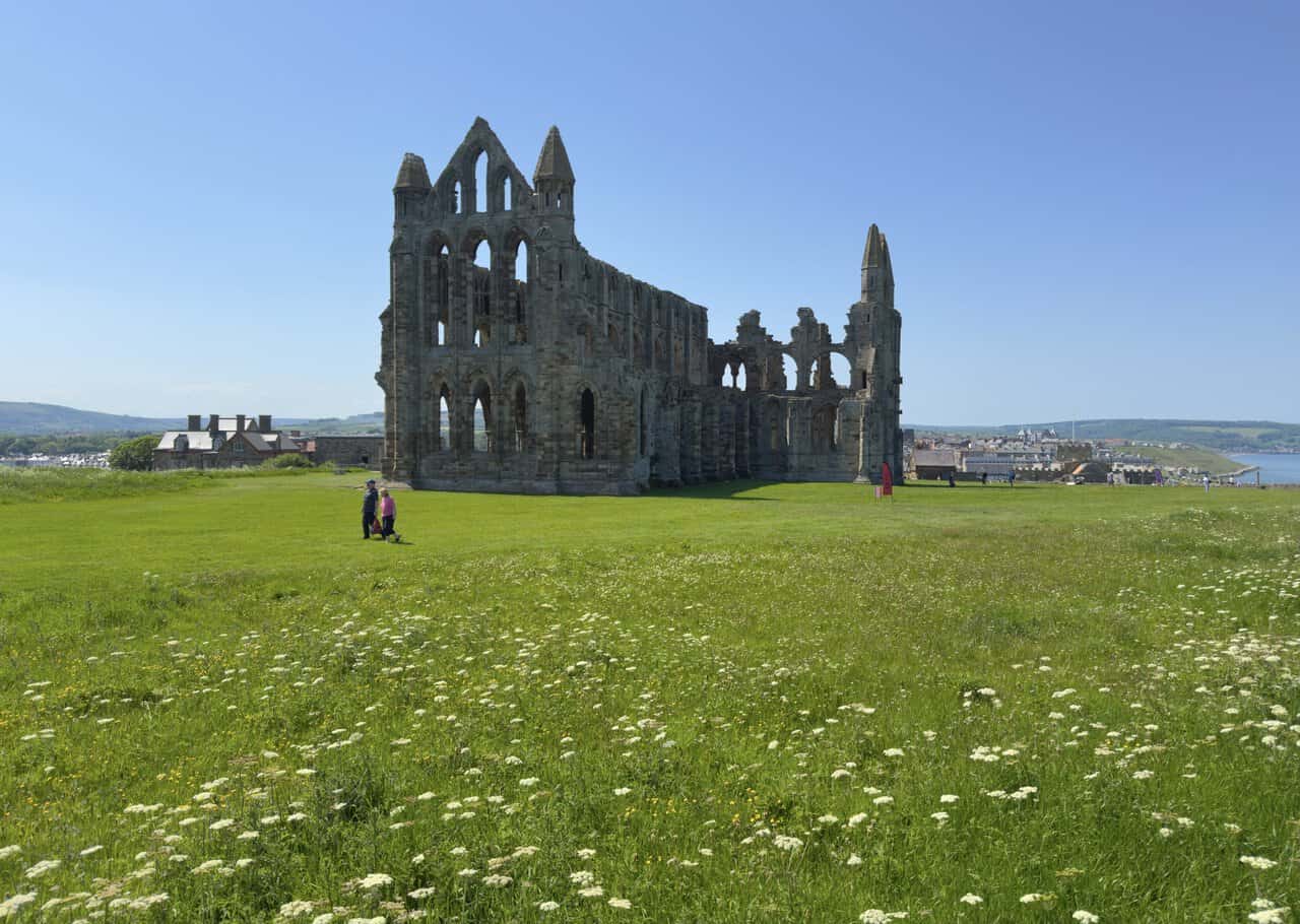 The ruins of Whitby Abbey stand behind a high stone wall, showing the scale of the former Benedictine abbey.