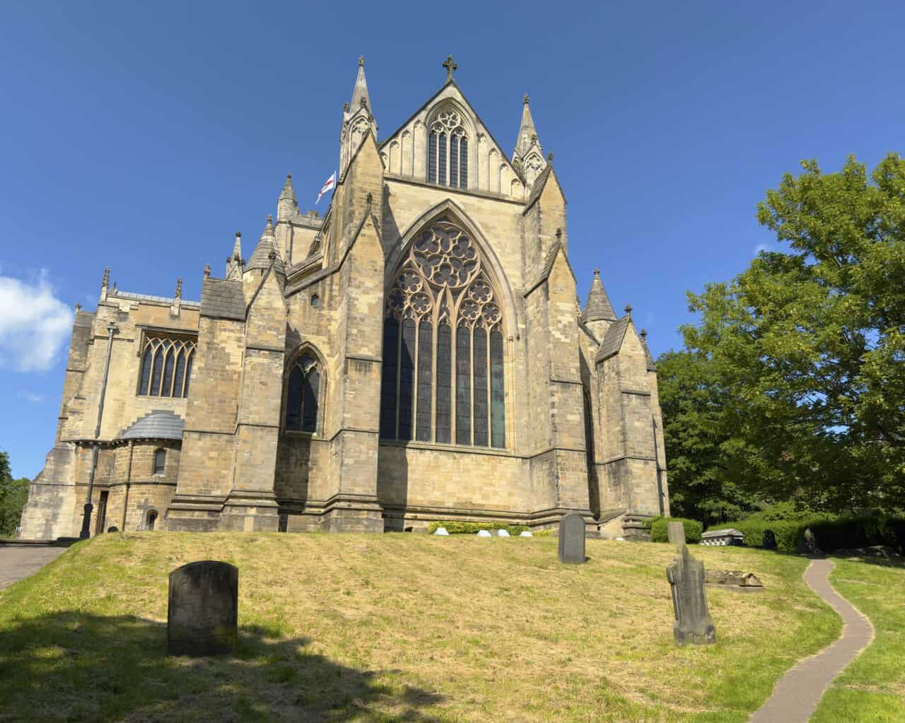 Ripon Cathedral viewed from the sloping churchyard on a Ripon walk, with its large traceried window and rose window above.
