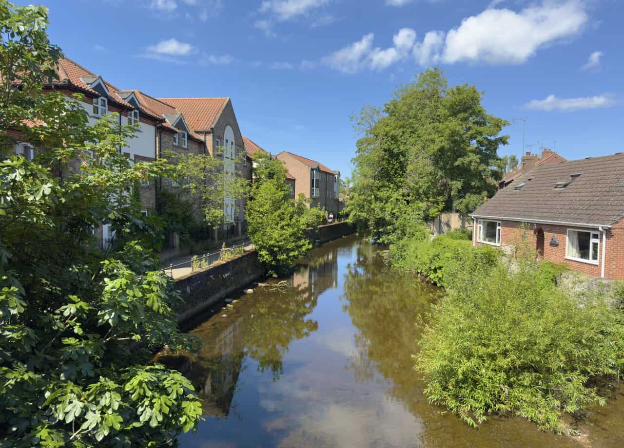 The River Skell at Bondgate Bridge on a Ripon walk, with calm water, trees and riverside buildings reflected on the surface.