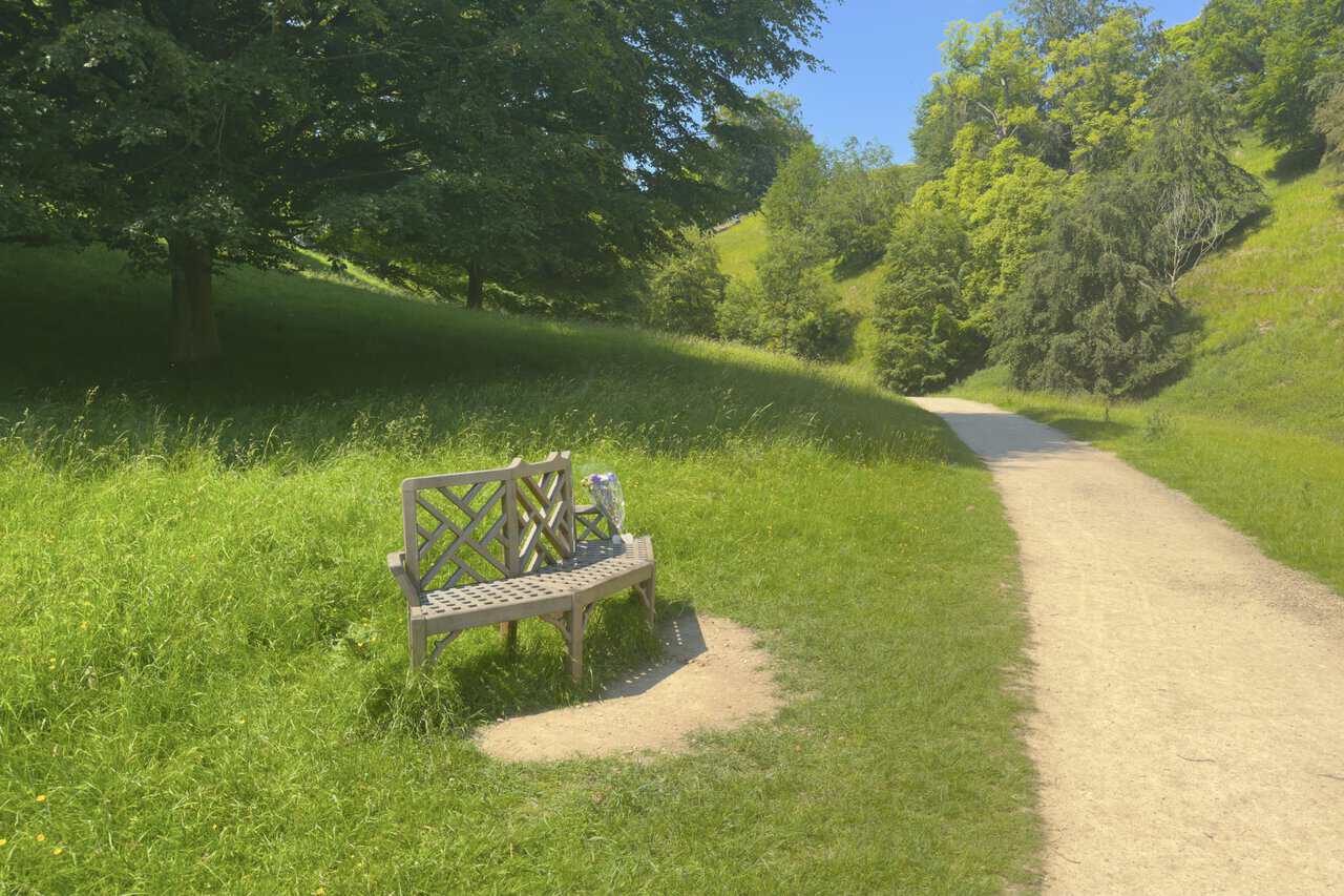 A wooden bench with flowers beside the path in the quiet valley near Chinese Wood and Mackershaw.