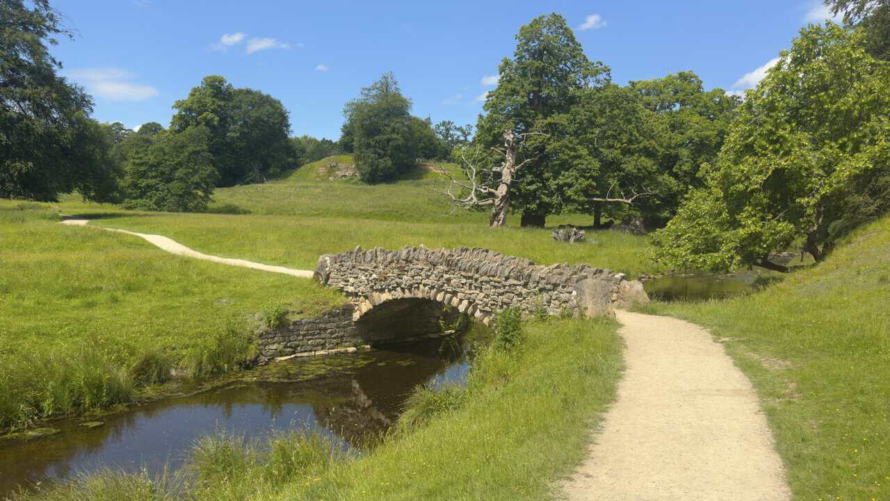 A low stone bridge reflected in the River Skell on a Ripon walk as Seven Bridges Valley opens into parkland.