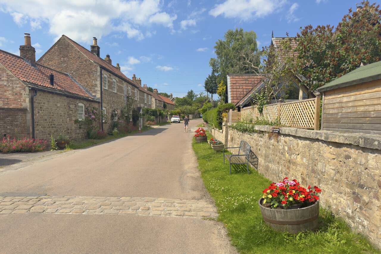 The village of Studley Roger, with stone cottages, red pantile roofs, flowers and garden walls along the lane.