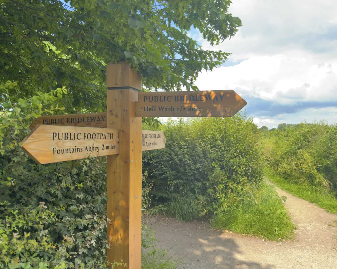 A wooden fingerpost near Studley Roger, signposting paths towards Fountains Abbey, Ripon and Hell Wath.