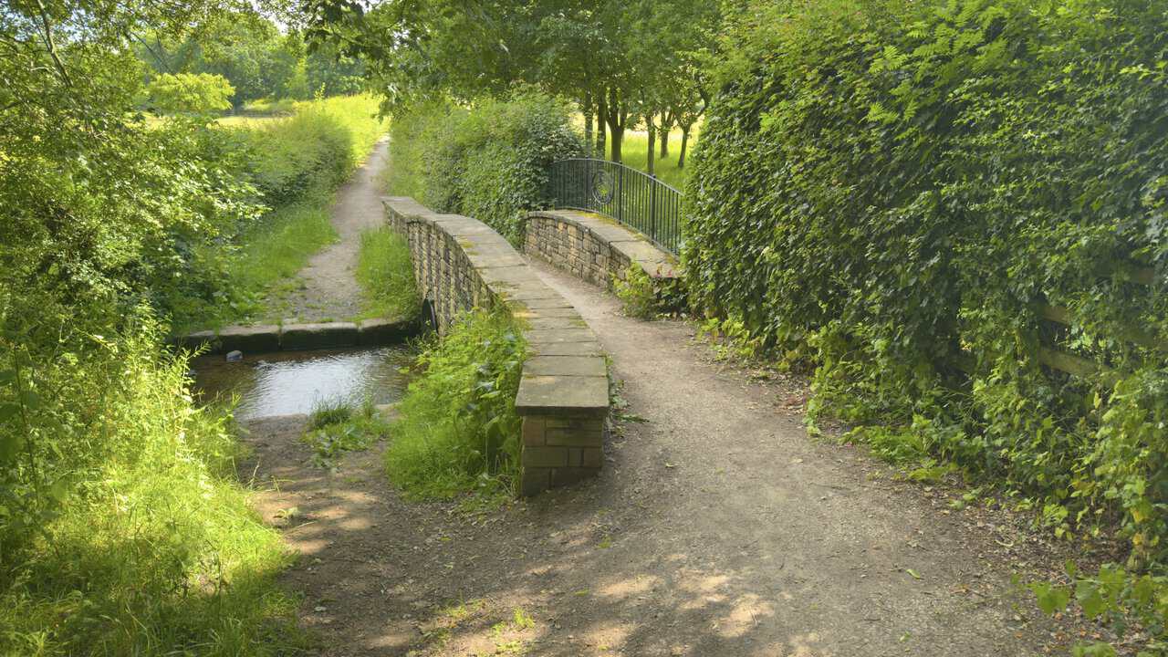 A small stone bridge on a Ripon walk, with curved iron railings crossing a stream on the bridleway near Studley Roger.