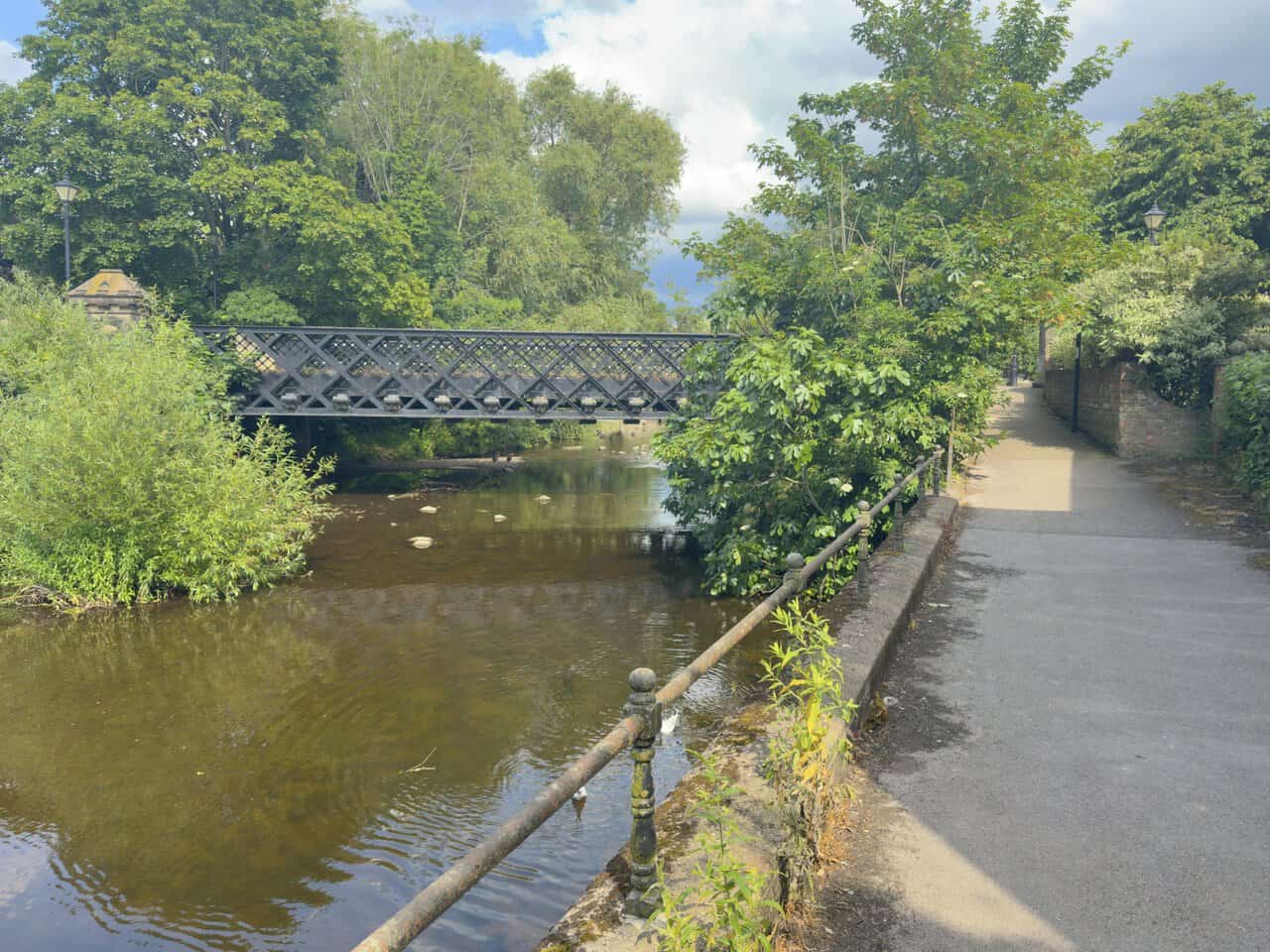 Bondgate Bridge on a Ripon walk over the River Skell in Ripon, showing its black iron lattice-girder span and riverside railings.