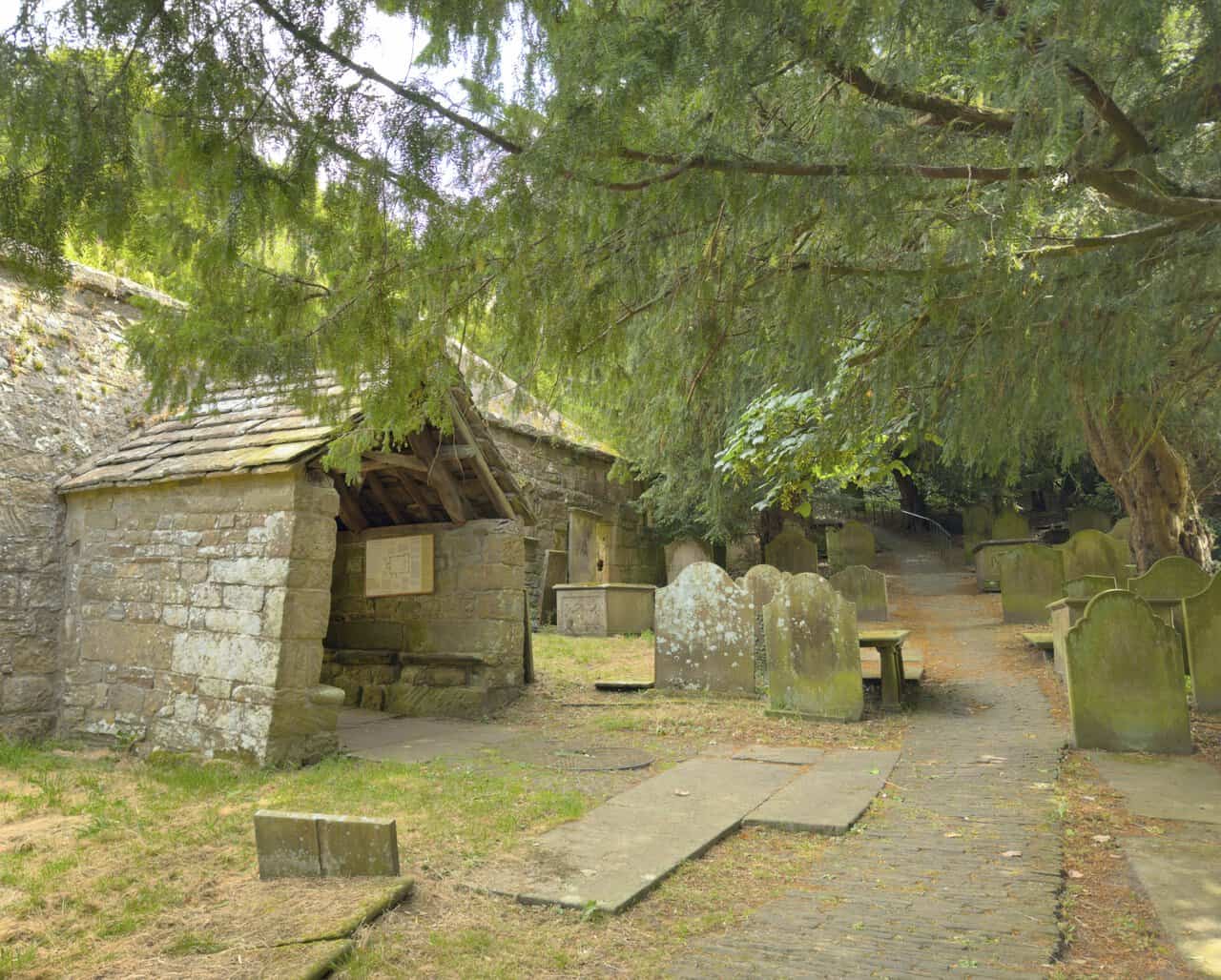 Ancient yew tree, historic gravestones and the stone south porch in Saint Mary’s churchyard.