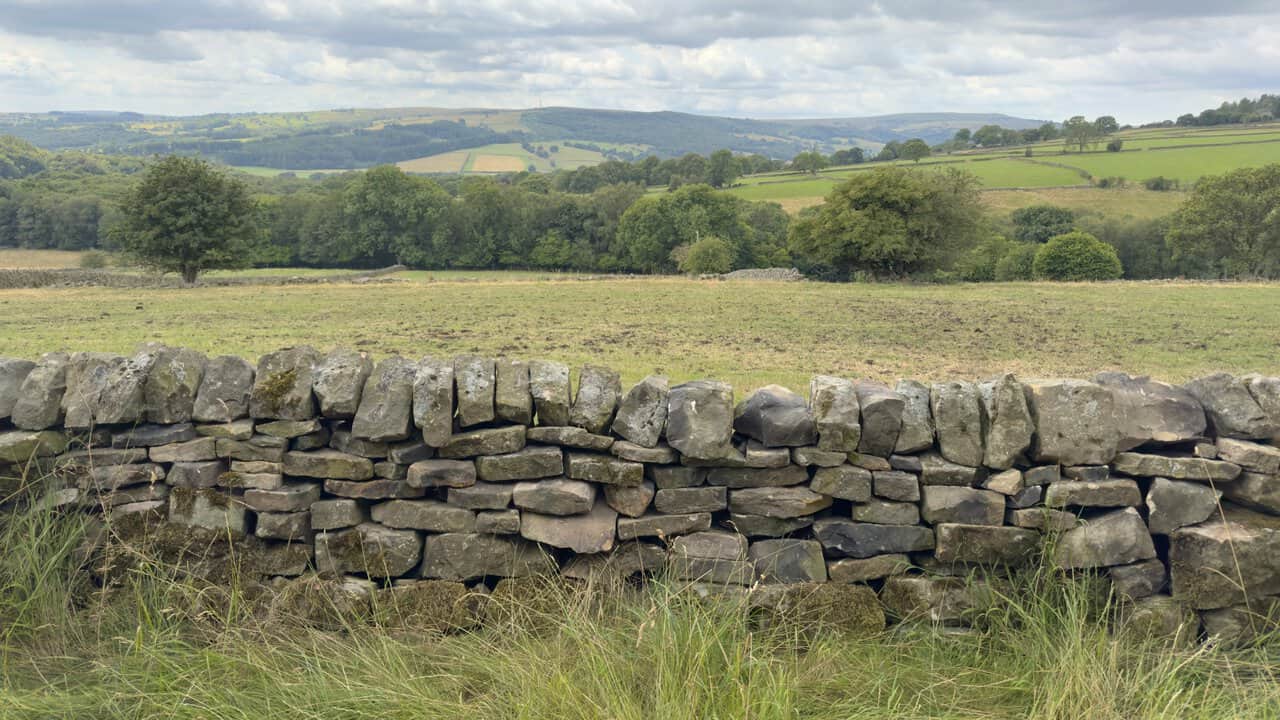 Wide stone track climbing above green fields, woodland and distant moorland hills.