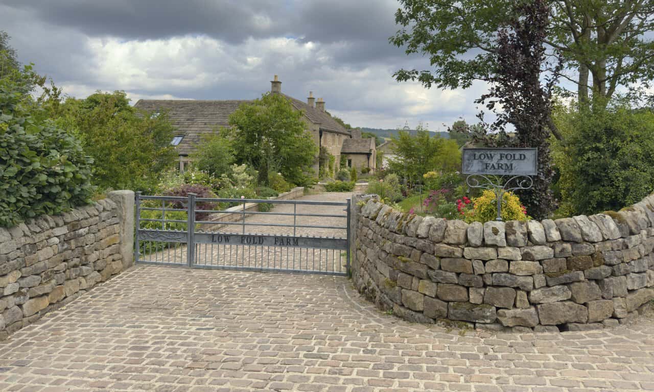 Low Fold Farm in Glasshouses, with a cobbled drive, colourful borders and traditional stone farmhouse.