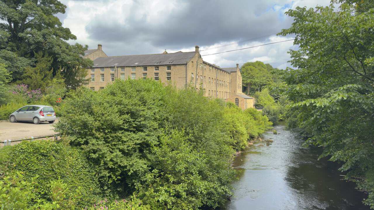 Glasshouses Mill beside the River Nidd, showing its large stone exterior and converted riverside buildings.