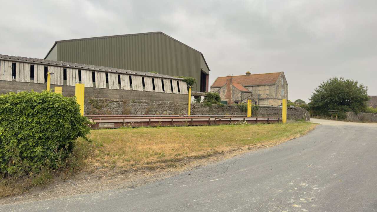 The tarmac lane at Whitcliffe Hall, with a weighbridge and yellow posts, a corrugated barn and the stone farmhouse beyond.