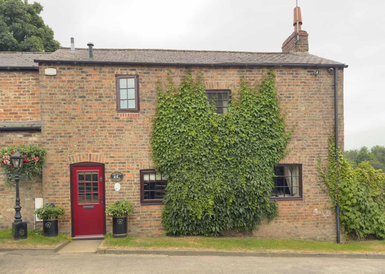 Hell Wath Cottage, a brick house clad in Virginia creeper, with a bright red door, hanging baskets and an old-fashioned lamp post.