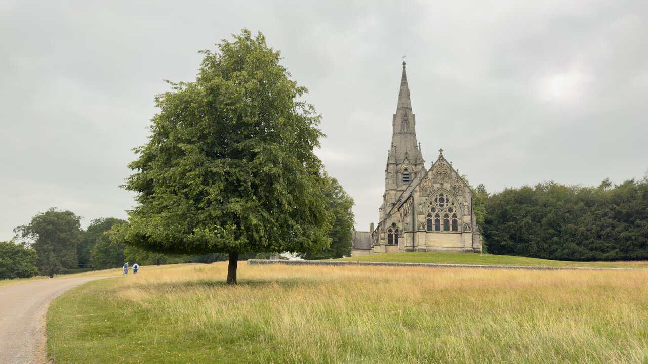 The hard-surfaced path on the Fountains Abbey circular walk approaching St Mary's Church, a lone tree framing the view across the meadow.