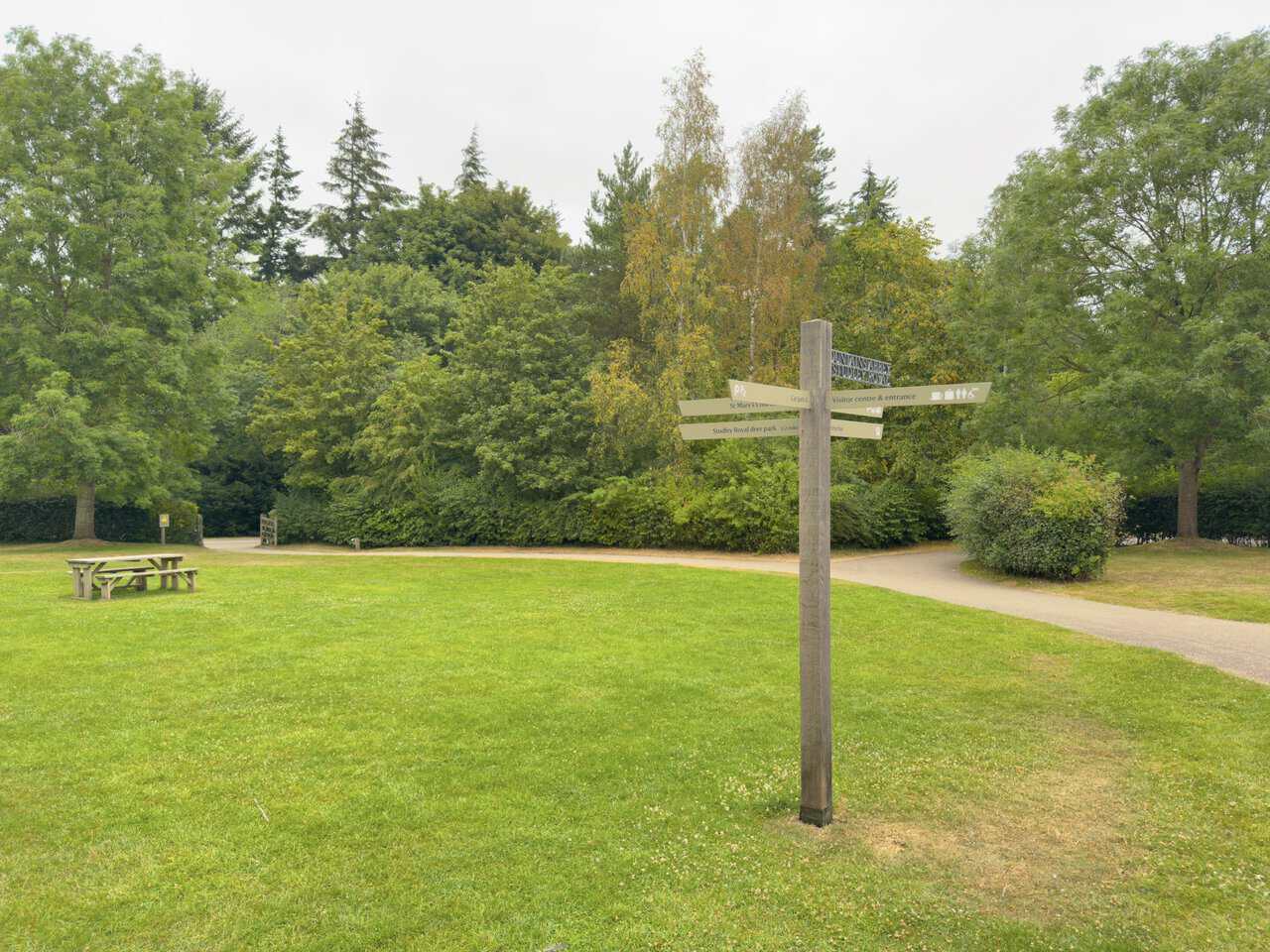 A wooden signpost on the grassy picnic area pointing towards St Mary's Church and Studley Royal deer park.
