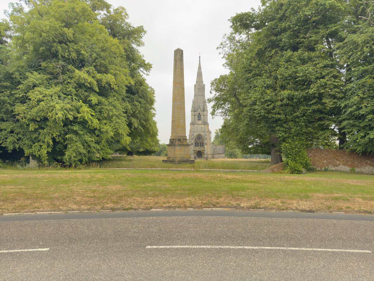 The stone obelisk in the foreground, with the spire of St Mary's Church rising behind it across the parkland.