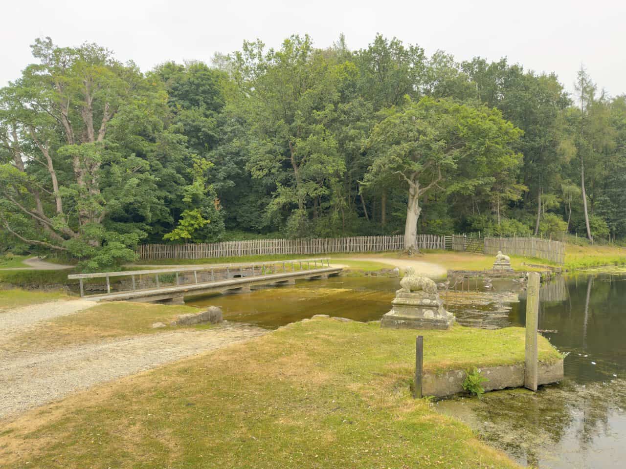 The footbridge over the lake outflow, flanked by a stone sphinx, where the Seven Bridges Valley section of the Fountains Abbey walk begins.