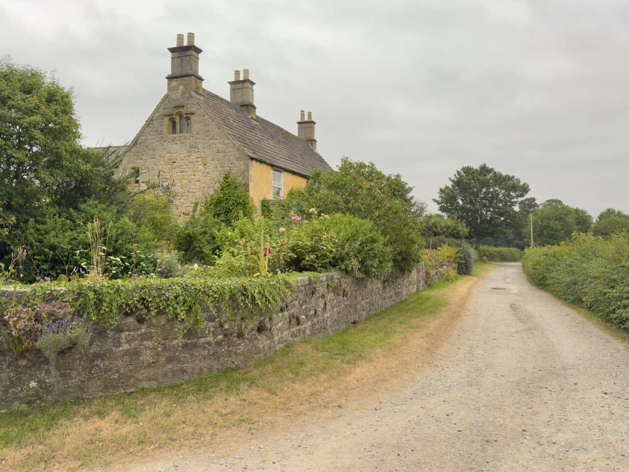 Plumpton Hall, a mid seventeenth-century stone farmhouse with tall chimneys and a flower-filled cottage garden.