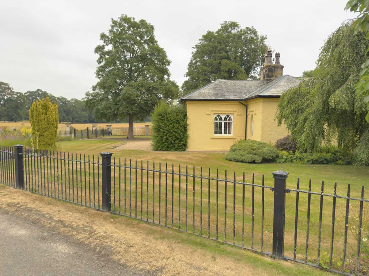 Studley Lodge, a single-storey yellow-rendered lodge with Gothic-style windows, set behind black iron railings.