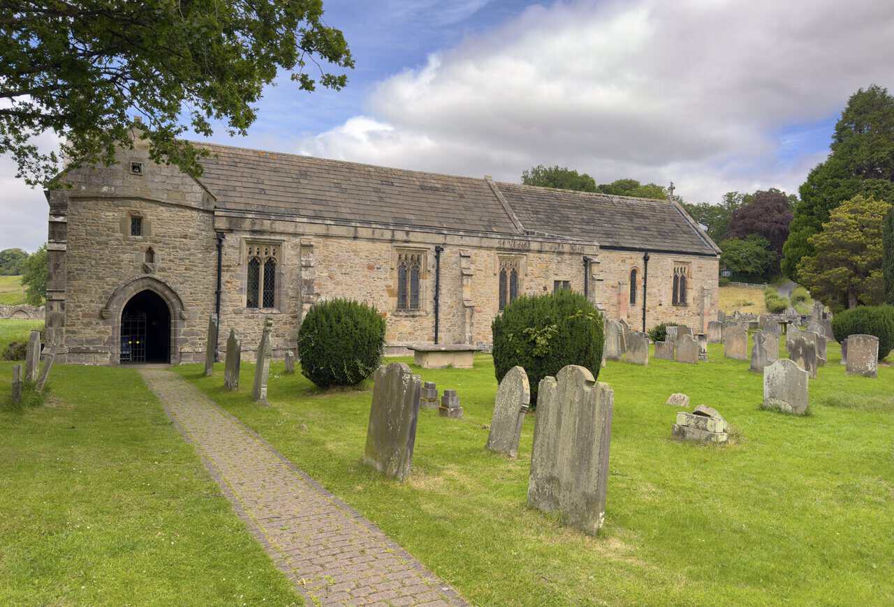 St Agatha’s Church at Easby, with a stone-slate roof, cobbled path, churchyard and arched south doorway.