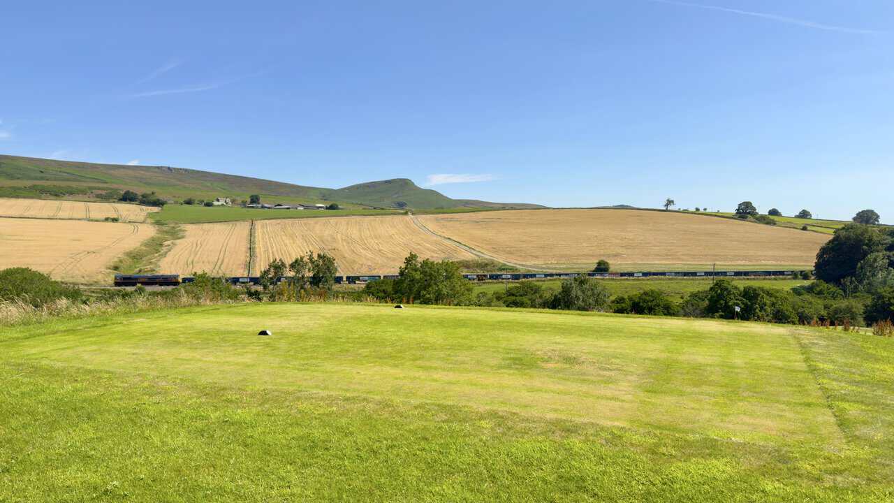 Embsay Crag above Embsay Moor with a freight train passing between stubble fields and the golf course.
