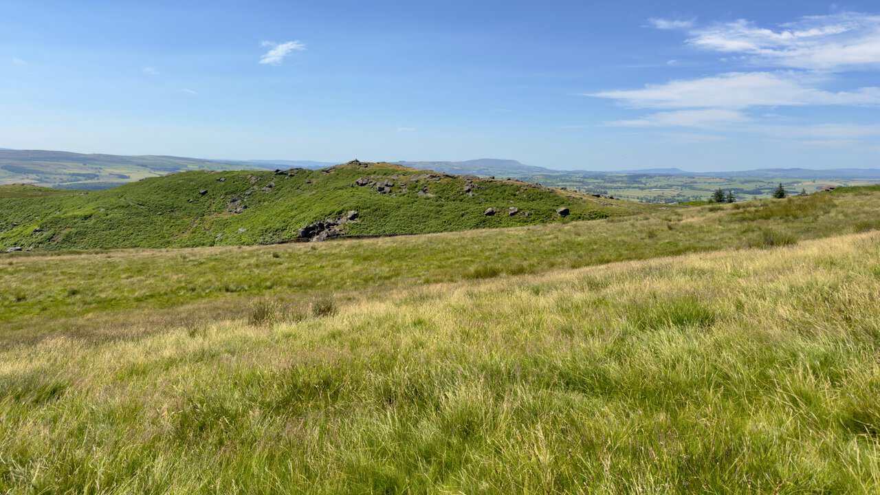 Bracken-covered hill with a small summit cairn, and the silhouette of Pendle Hill on the horizon.