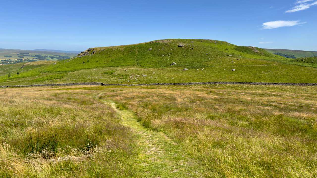 Grassy path descending to a dry stone wall below Rough Haw on Flasby Fell.
