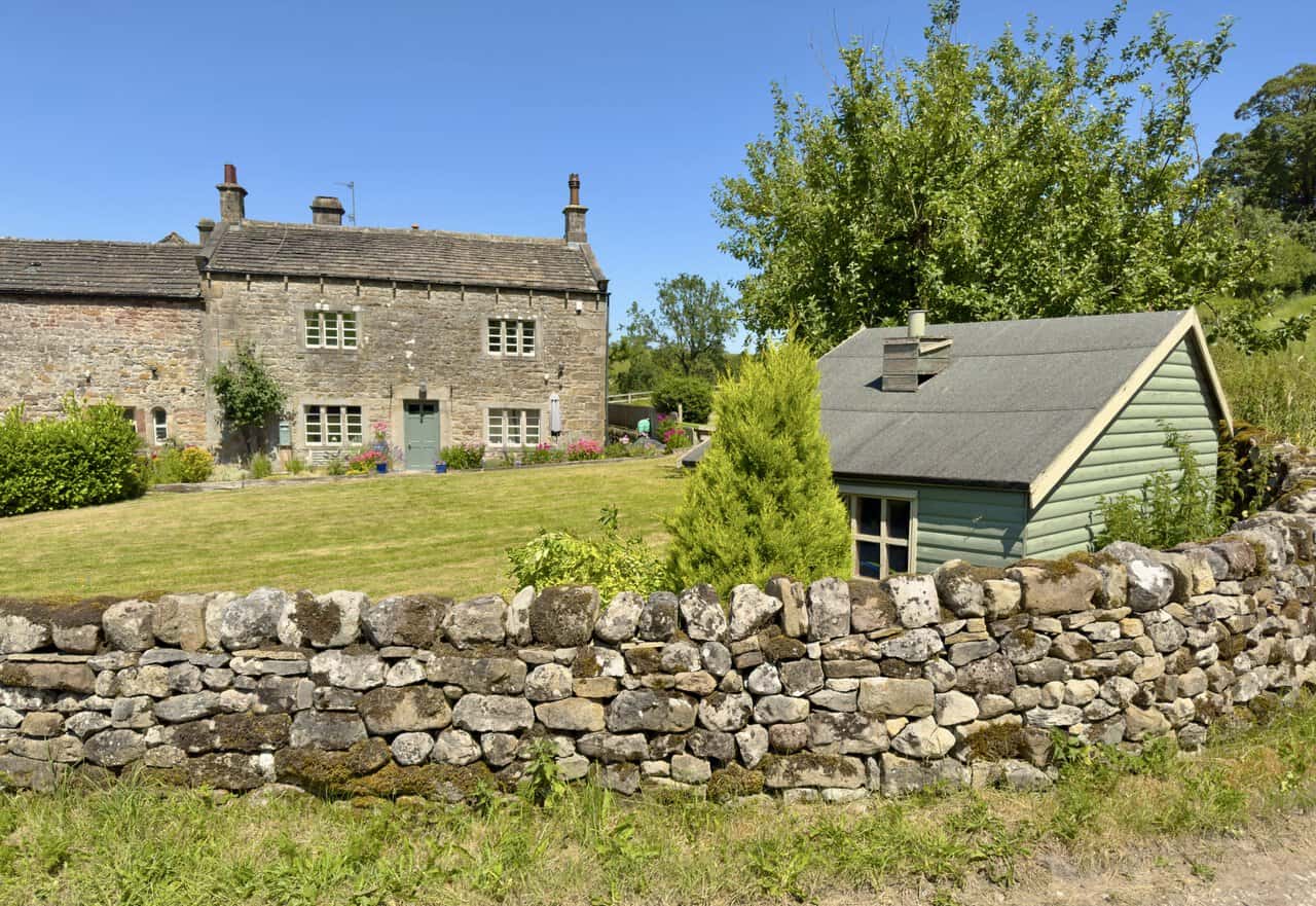 Stone farmhouse with mullioned windows behind a dry stone wall in the hamlet of Flasby.