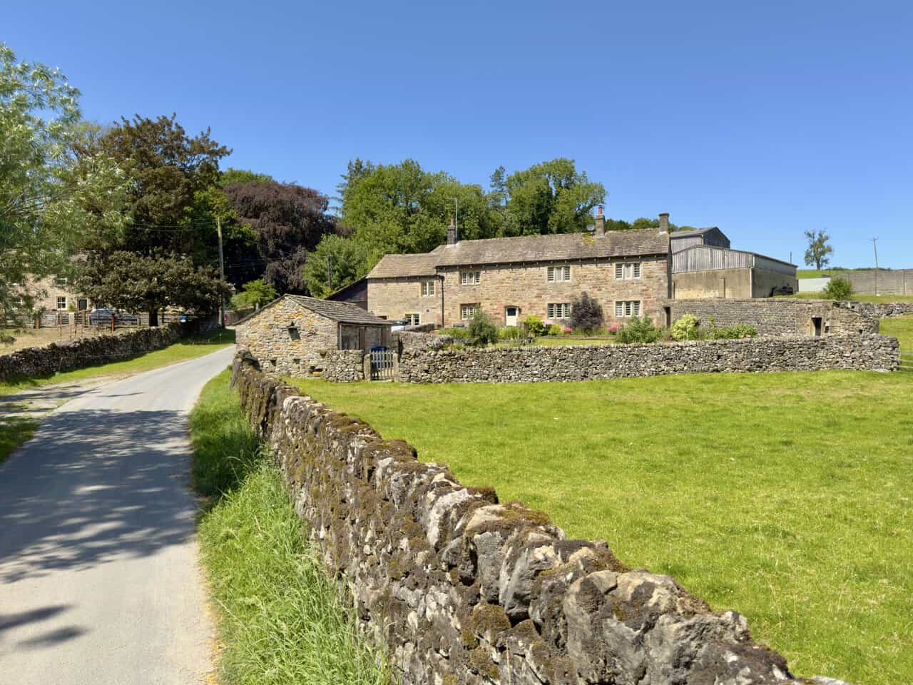 Quiet tarmac lane through Flasby past a small stone barn and a long gritstone farmhouse.
