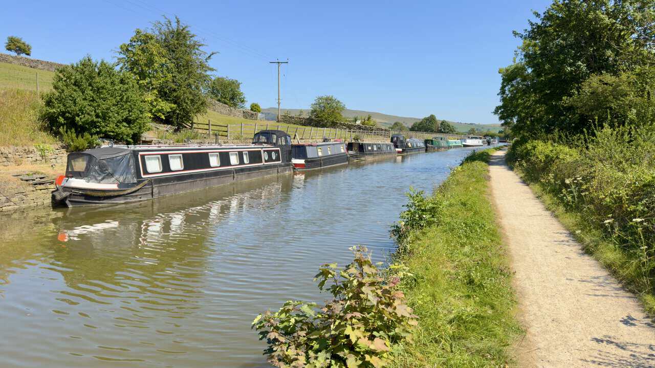 Narrowboats moored nose to tail along the Leeds and Liverpool Canal approaching Skipton.