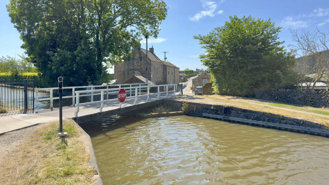 Niffany Swing Bridge over the Leeds and Liverpool Canal, with stone houses on the slope beyond.