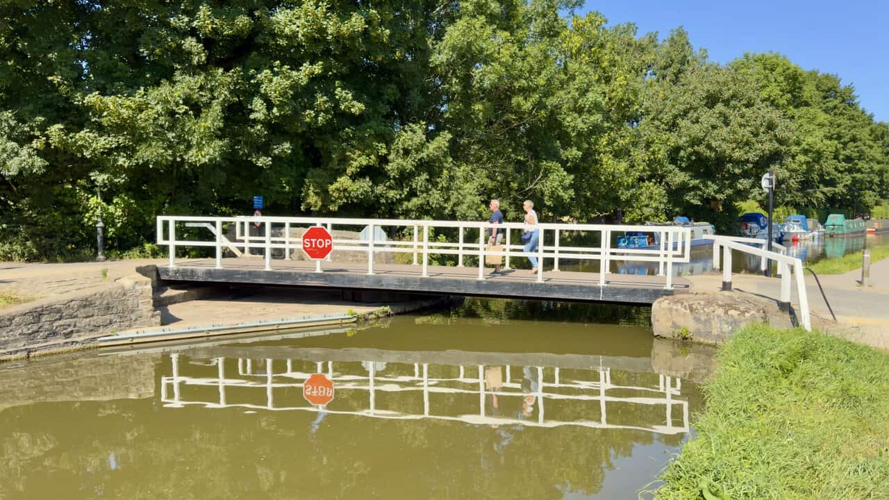 Swing bridge on the Leeds and Liverpool Canal reflected in the water, with walkers crossing.
