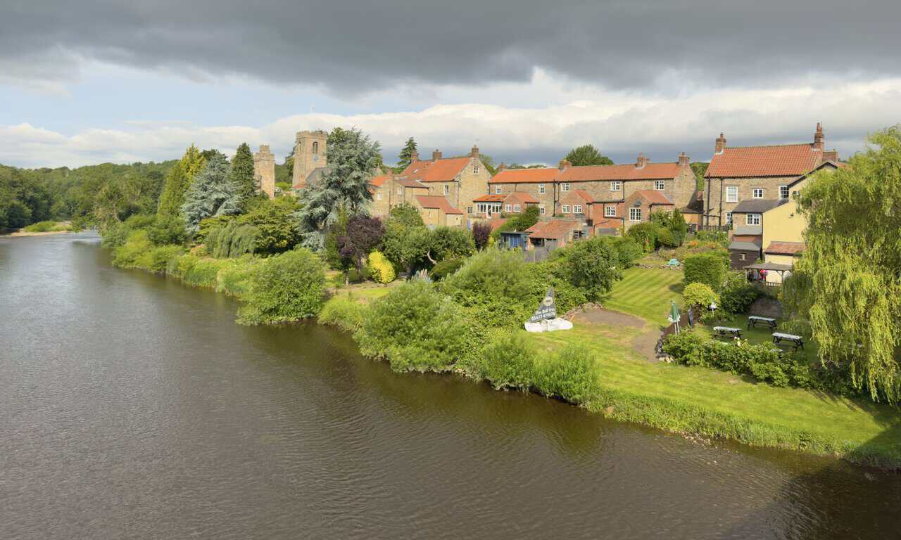Upstream view from Tanfield Bridge showing riverside cottages, the Bull Inn garden, St Nicholas’s Church and Marmion Tower.