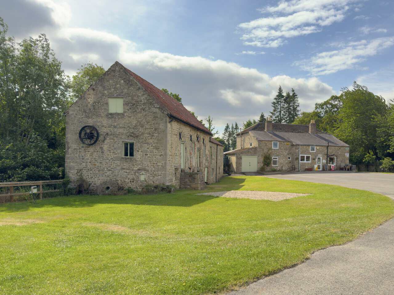 Historic stone watermill and iron waterwheel beside the reception building at Sleningford Water Mill Caravan and Camping Park.