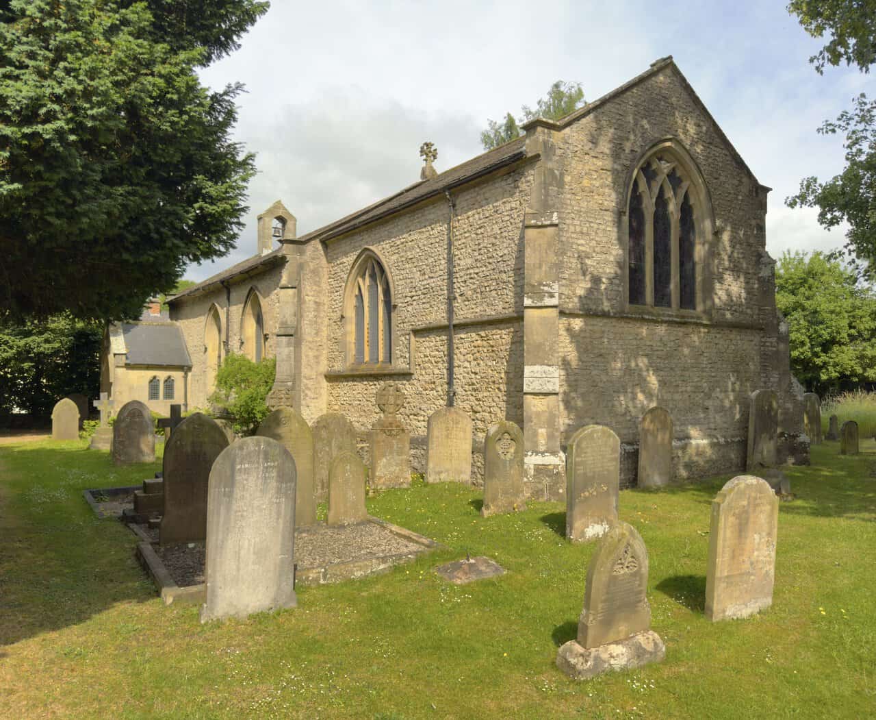 St Mary the Virgin Church in North Stainley, surrounded by trees and a sloping churchyard filled with weathered gravestones.