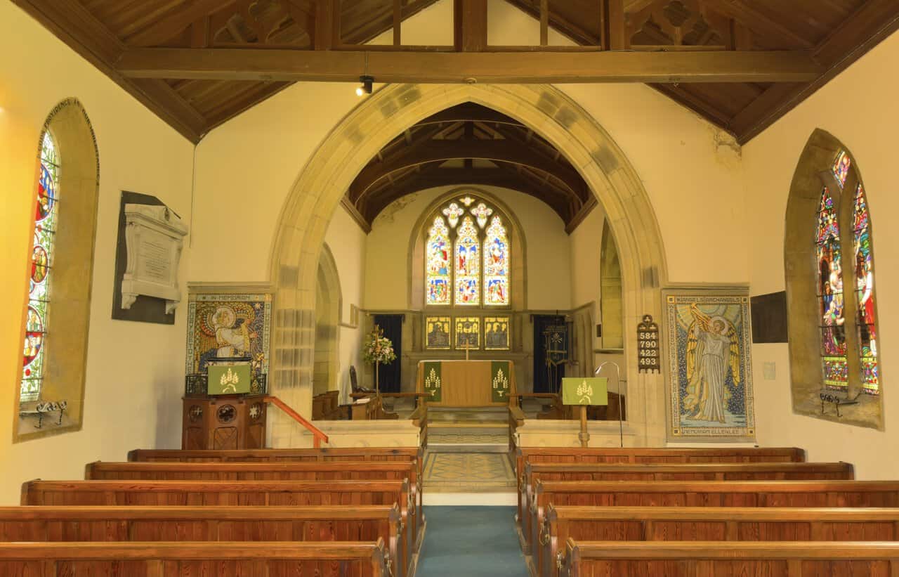 Interior of St Mary the Virgin Church with wooden pews, a timber roof, stained-glass windows and gilded angel memorial panels.