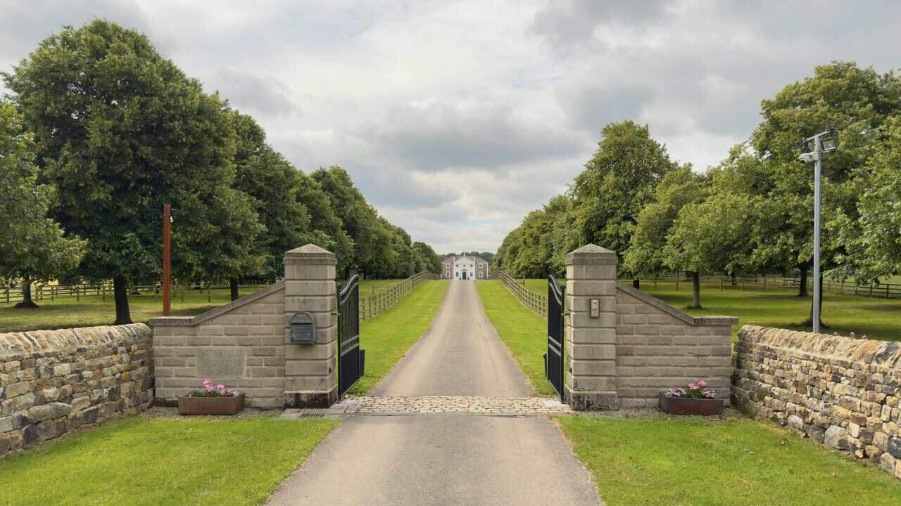 Stone gateposts at Newfield Farm framing a tree-lined drive and distant country house on the West Tanfield walk.
